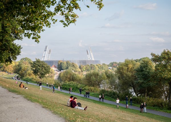 Menschen spazieren und sitzen auf der Weserpromenade in Bremen mit Blick auf das Weserstadion