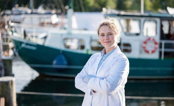 Junge Frau im weißen Kittel steht mit verschränkten Armen vor einem Bootsanleger